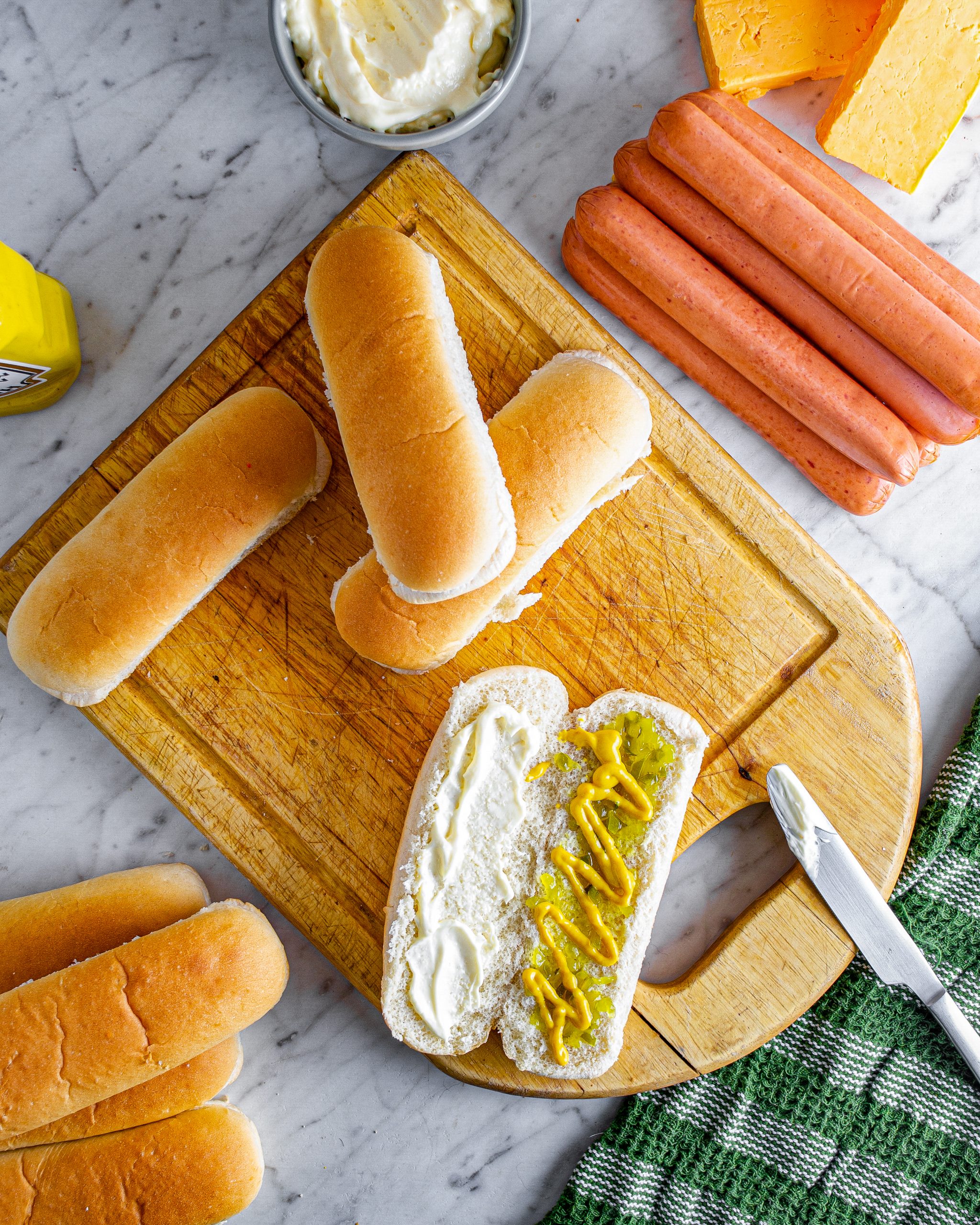 Spread relish, mustard, and mayonnaise to the inside of the hot dog buns. 