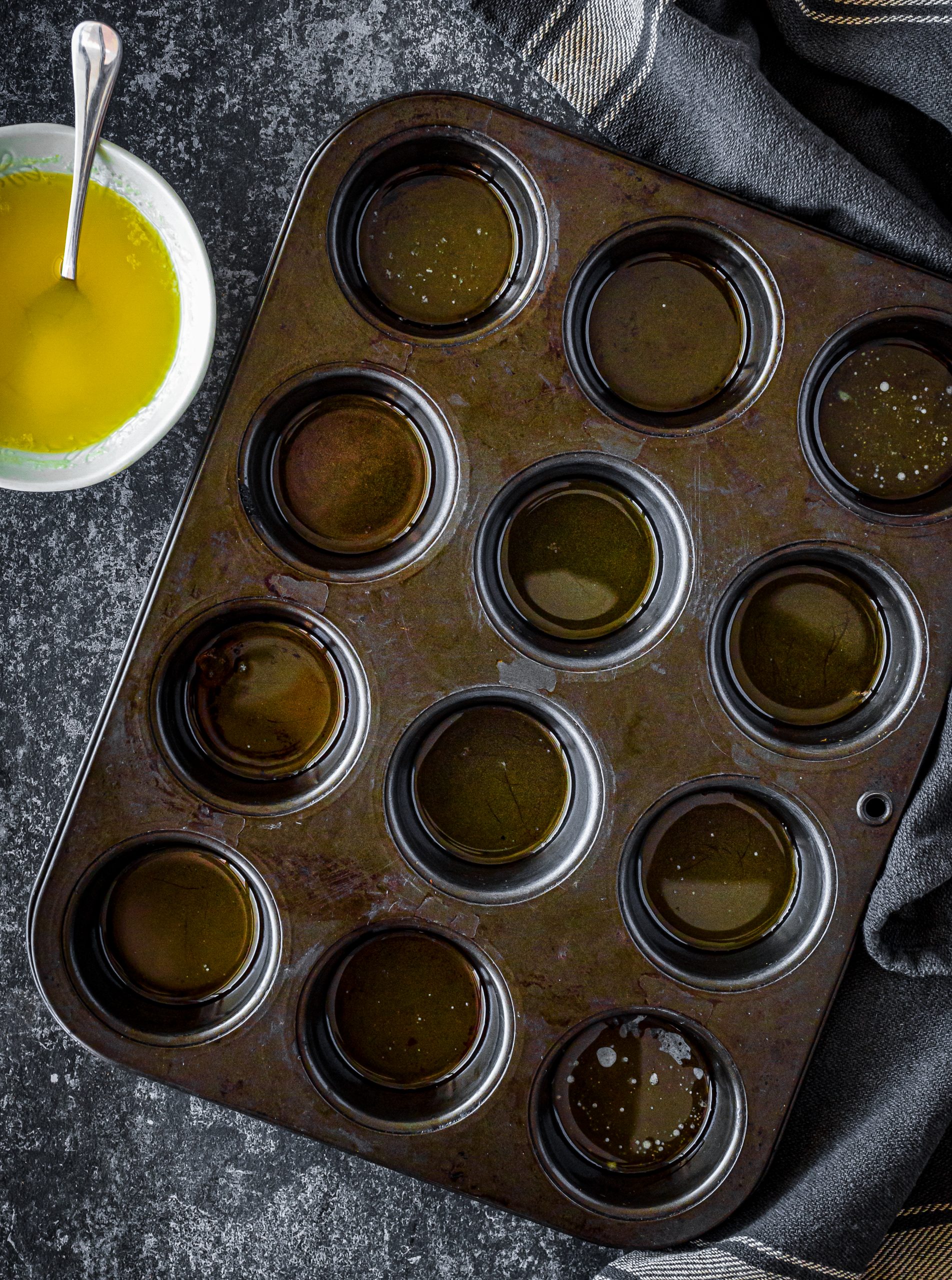 Melt the butter, and place a teaspoon of it into each of the sections of a muffin tin. 