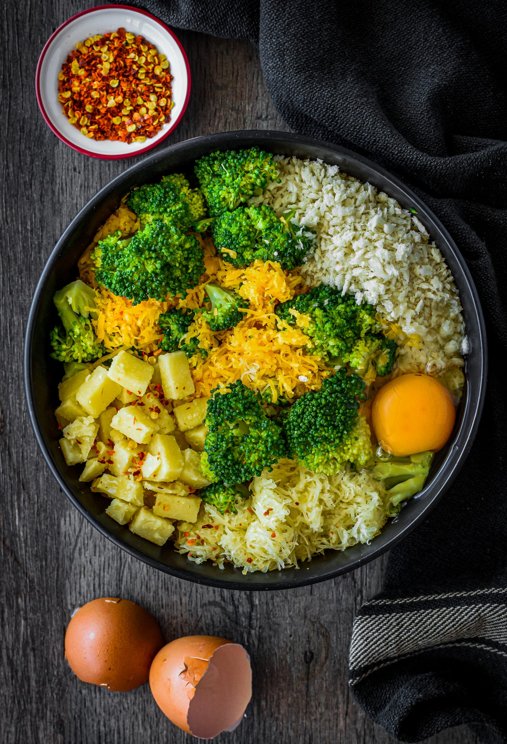  In a large mixing bowl, stir together the broccoli, velveeta, colby cheese, cheddar cheese, ¼ cup panko crumbs, red pepper flakes, 1 egg, and salt and pepper to taste. 